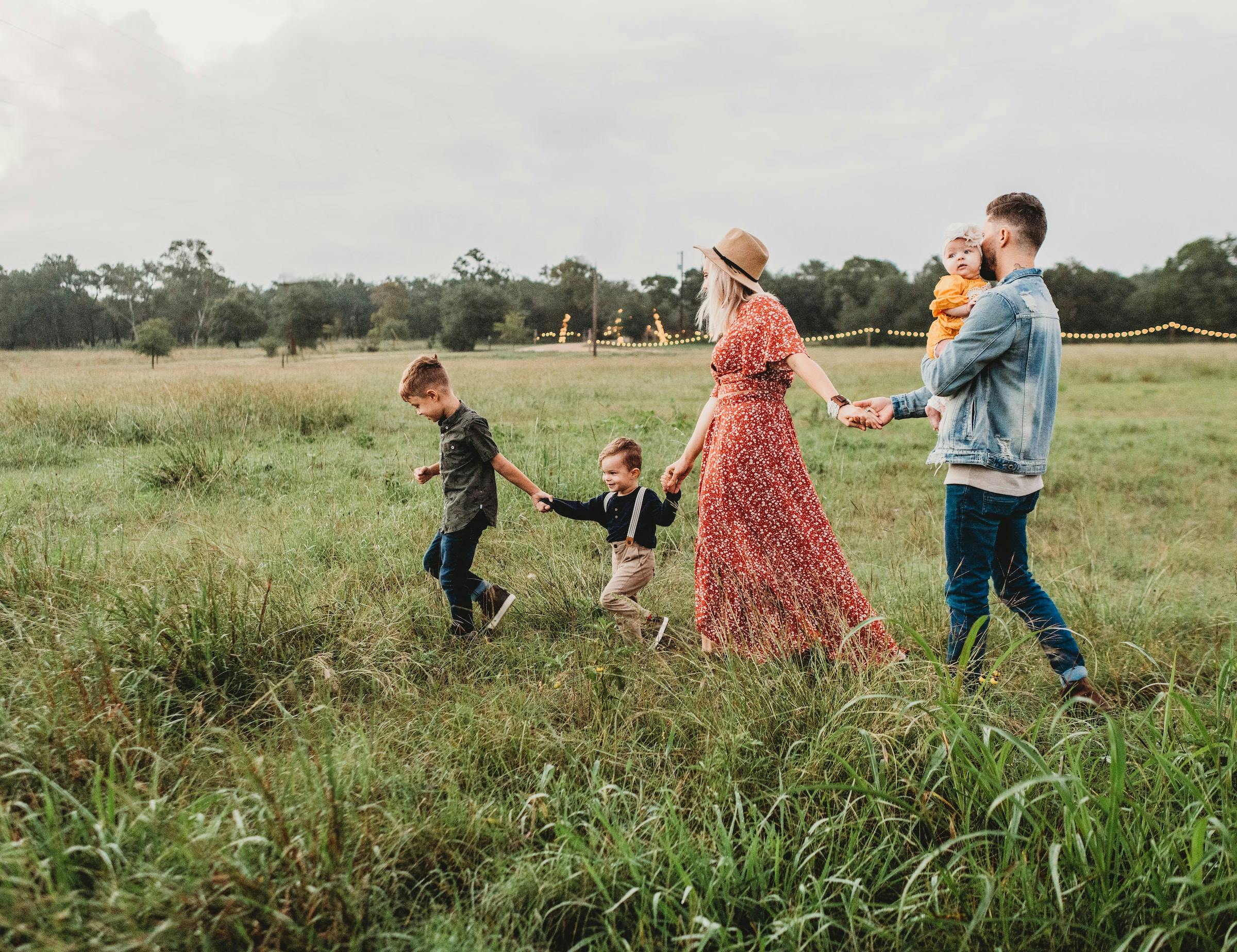 A family in simple, yet rustic clothing walking through a field of grass while holding hands.